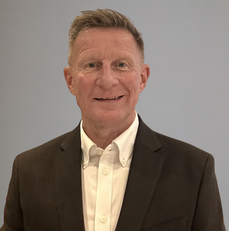 John Evans A man in a suit smiling against a plain background.