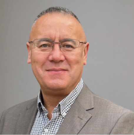 Phil Choi Smiling man in a grey suit with glasses and short, grey hair against a neutral background.